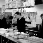 Black and white company of female cooks preparing food in kitchen of cafe while interacting and smiling